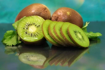 Bright Hd Photo Of A Set Of Sappy Kiwi Slices Leaning On A Pair Of Unpeeled Whole Kiwis On Top Of A Reflective Surface