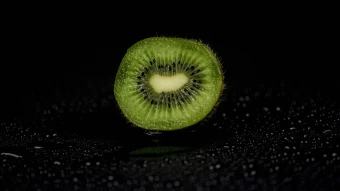 Luscious Fruit Photography Of The Core Of A Kiwi Cut In Half At Center Frame Of A Black And Wet Plane