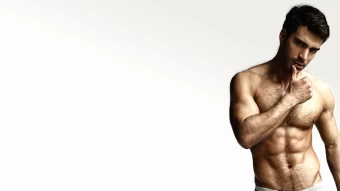 Shirtless Muscular Man Flexing His Muscles While Doing A Seductive Pose Against A White Background.