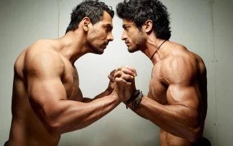 Two Muscular Men Grappling While Facing Each Other Against A White Background
