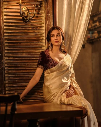 Embracing elegance and grace, Saumya Tandon radiates beauty in a timeless white sari while enjoying a moment of tranquility at the table.