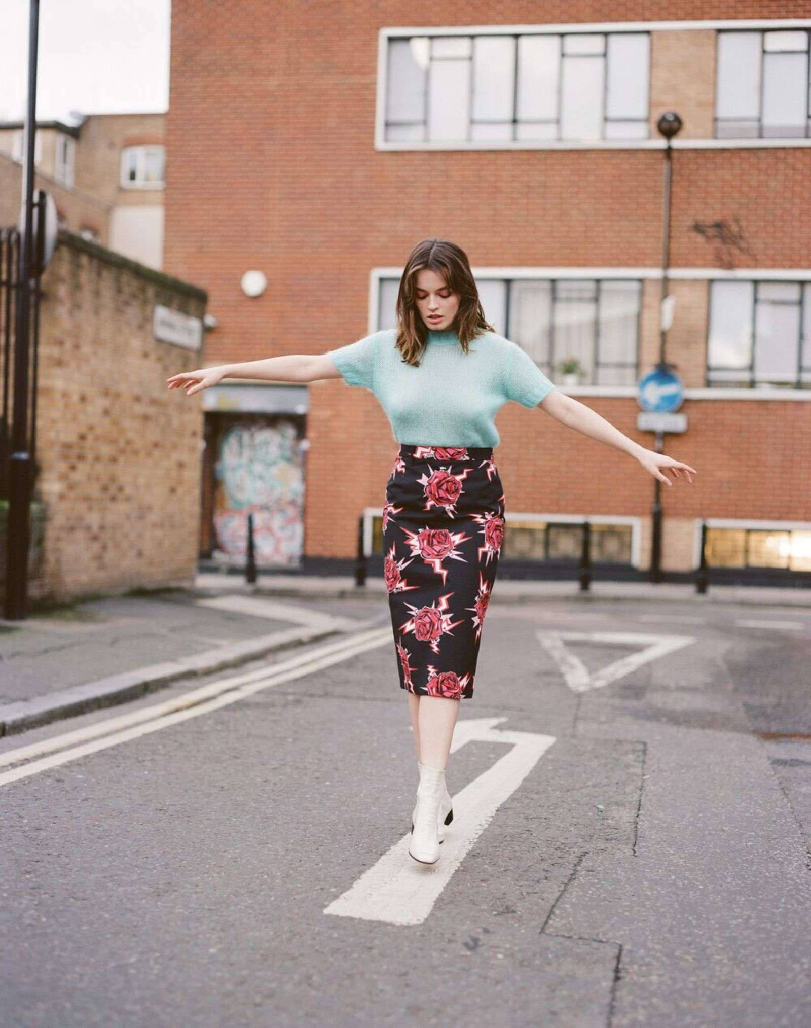A Fashion Editorial Featuring French Actress, Emma Mackey, Standing On A White Street Traffic Symbol In A Pretty Outfit.