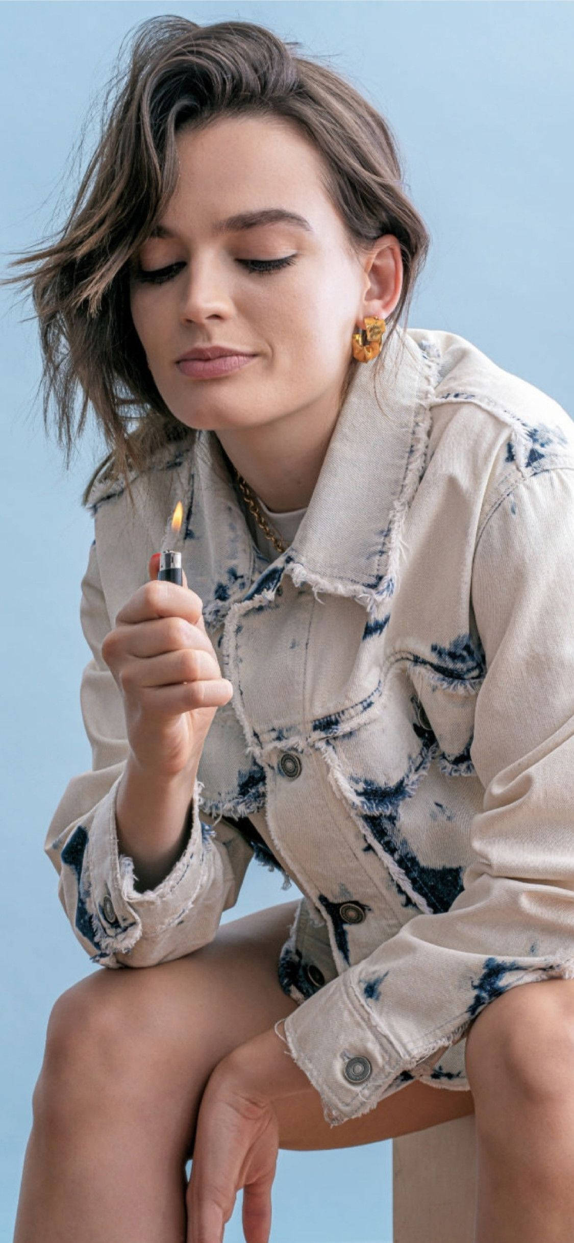 A Fashion Page Featuring The Popular Actress, Emma Mackey, Wearing An Acid Wash Top While Posing With A Lighter