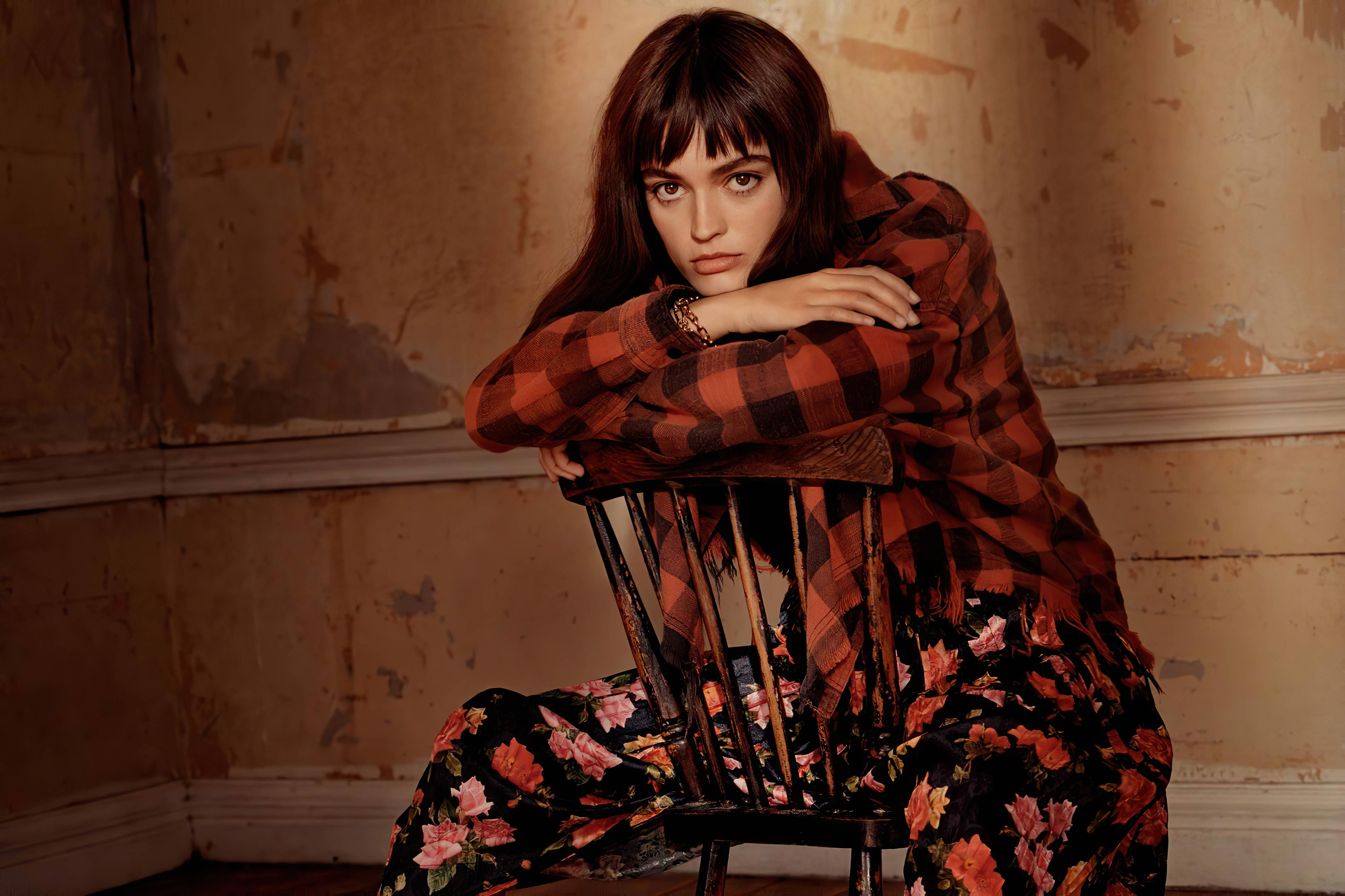 Editorial Portrait Of The Actress, Emma Mackey, With Bangs While Sitting Backwards On A Chair In Patterned Clothing