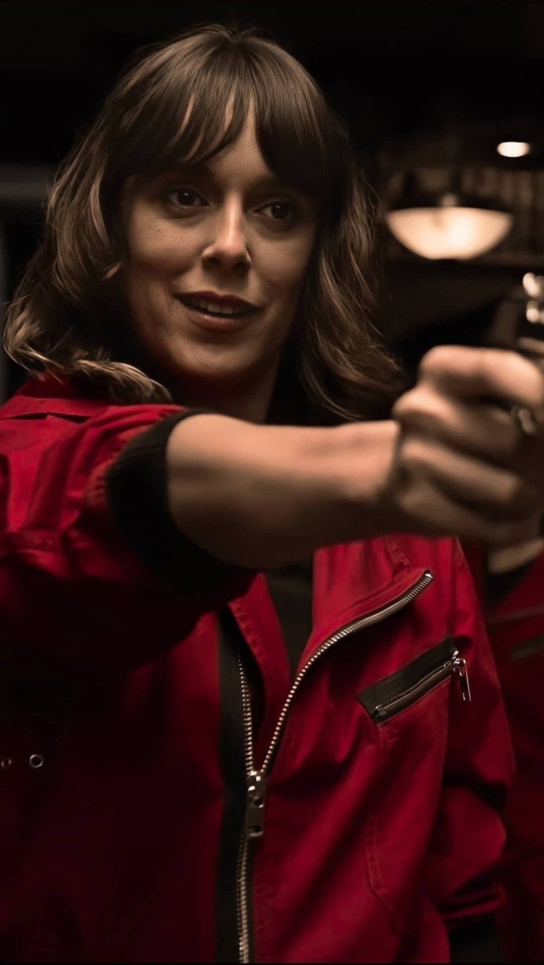 An Expressive Portrait Of Julia From Money Heist, Wearing A Red Jumpsuit As She Points Her Gun Toward Someone In Dark Background