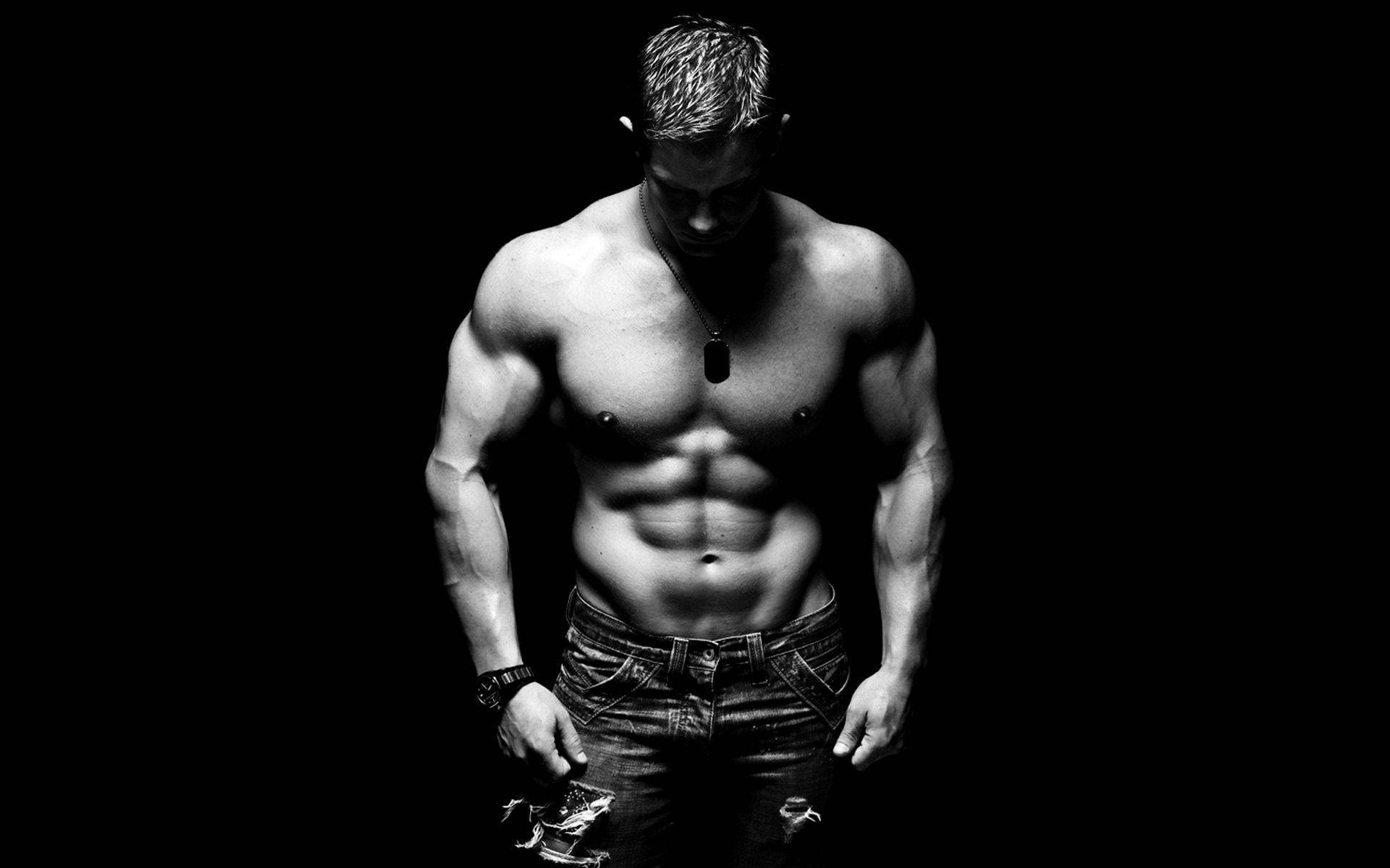 Black And White Photo Of A Shirtless Muscle Man Against A Dark Background