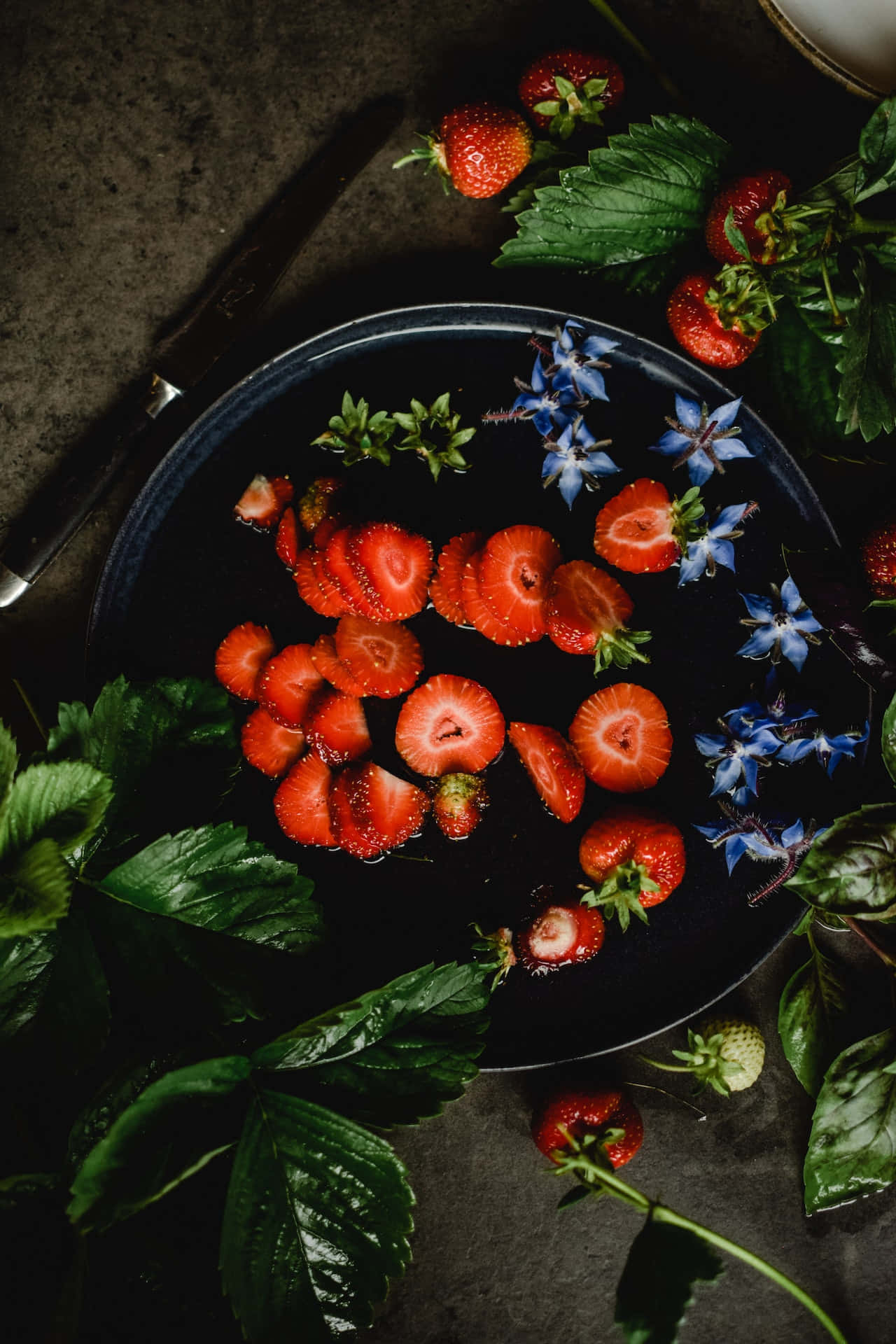 Phone Wallpaper Featuring A Photo Of Sliced Strawberries And Blue Borage Flowers On A Black Plate