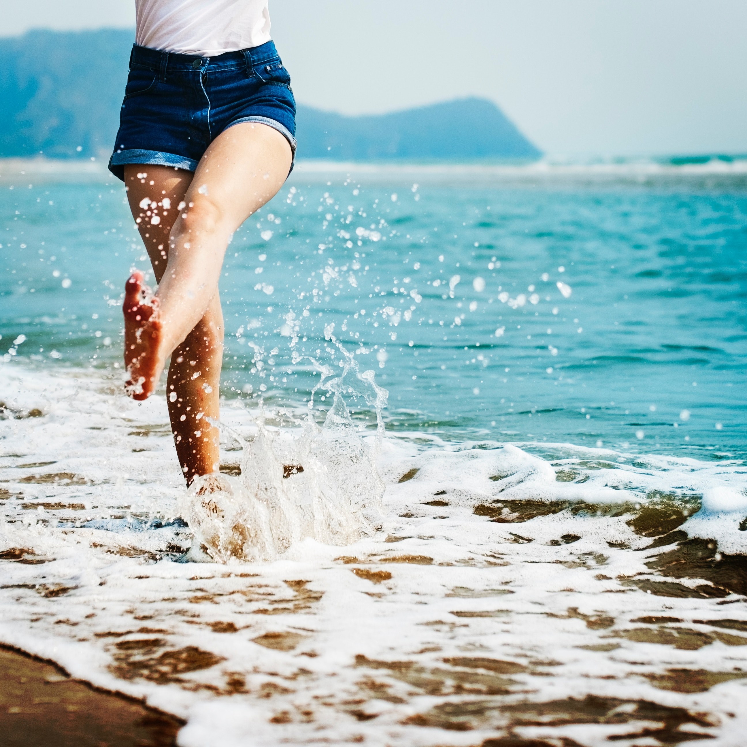a girl wearing jean shorts splashing her feet in the ocean, ocean splashing 4k wallpaper